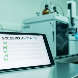 A professional, split-depth photography shot in a high-tech pharmaceutical laboratory. In the foreground, a focus-stacked view of a digital tablet displaying a "GMP COMPLIANCE AUDIT" checklist with green checkmarks, resting on a clean stainless steel surface. In the background, slightly out of focus, a scientist in full sterile PPE is interacting with a complex liquid chromatography instrument. The lighting is clinical, bright white and teal, emphasizing precision, cleanliness, and regulatory control.