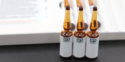 Three amber glass ampoules with white labels arranged in a row on a dark table, with a blurred document in the background.