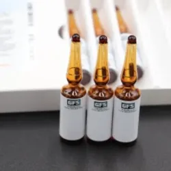 Three amber glass ampoules with white labels arranged in a row on a dark table, with a blurred document in the background.
