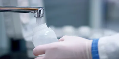 Scientist wearing blue gloves pipetting a sample into a microcentrifuge tube during PFAS analysis, with additional sample vials visible in the foreground