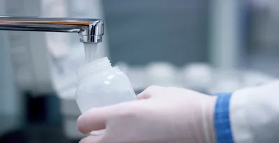 Scientist wearing blue gloves pipetting a sample into a microcentrifuge tube during PFAS analysis, with additional sample vials visible in the foreground