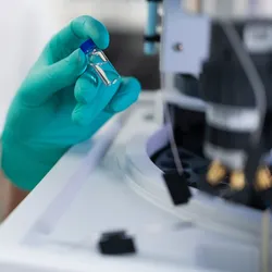 Laboratory researcher wearing protective gloves placing sample vial into high performance liquid chromatography system for chemical and clinical analysis.
