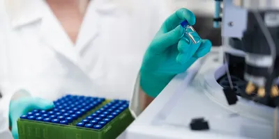 Laboratory researcher wearing protective gloves placing sample vial into high performance liquid chromatography system for chemical and clinical analysis.