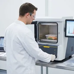 Scientist using a desktop XRF analyzer to test food packaging materials like plastic and cardboard for trace metals in a laboratory.
