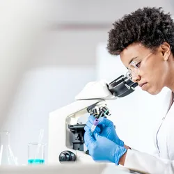 Female scientist marking a test tube next to a microscope