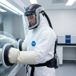 Laboratory technician in full protective equipment (PPE) working in a glovebox to handle nanomaterials safely during particle analysis