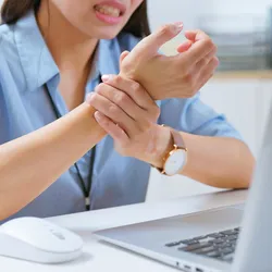 Individual showing signs of repetitive strain injury at desk