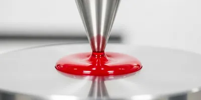 Close-up of a red liquid droplet being tested with a viscometer