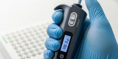 A close-up of a gloved hand holding a sleek, modern electronic pipette.
