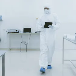 Scientist Using Digital Tablet Computer and wearing Protective Suit walks through Manufacturing Laboratory