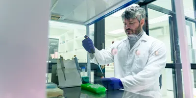 Scientist in a lab wearing a lab coat and using a pipette in a fume hood, representing Shut the Sash competitions.