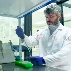Scientist in a lab wearing a lab coat and using a pipette in a fume hood, representing Shut the Sash competitions.