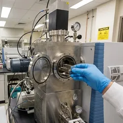 Scientist loading a material sample into a mass spectrometry instrument in a laboratory for surface analysis.