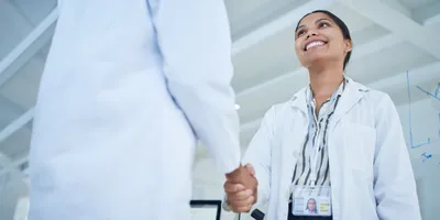 A woman in a lab coat shakes hands in a professional setting