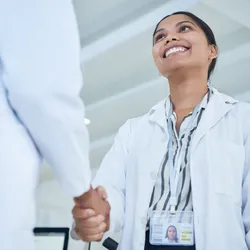 A woman in a lab coat shakes hands in a professional setting