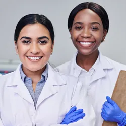 Three women in lab coats smiling together, representing women in leadership.