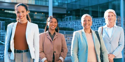Four women leaders standing outside corporate building smiling at camera, representing women leaders in STEM