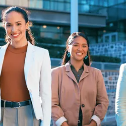 Four women leaders standing outside corporate building smiling at camera, representing women leaders in STEM