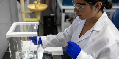side-view of a woman scientist weighing a solid white sample on a scale