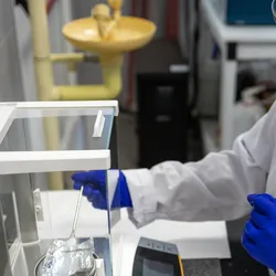 side-view of a woman scientist weighing a solid white sample on a scale