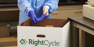 Lab technician placing blue gloves into an Ansell RightCycle recycling bin.
