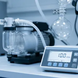 Professional digital vacuum controller displaying 10.0 mbar on a laboratory benchtop, connected to a diaphragm vacuum pump and rotary evaporator glassware in a clean chemistry lab.