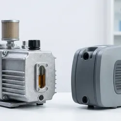 Comparative photograph of an industrial rotary vane vacuum pump with an oil sight glass and a modern oil-free diaphragm laboratory pump on a benchtop.