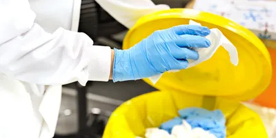 A lab worker discarding plastic waste into a yellow bin, highlighting lab sustainability efforts.