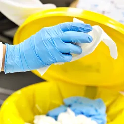 A lab worker discarding plastic waste into a yellow bin, highlighting lab sustainability efforts.