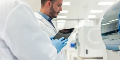 Two scientists wearing lab coats and gloves are using a digital tablet in a modern laboratory, conducting medical research with advanced equipment