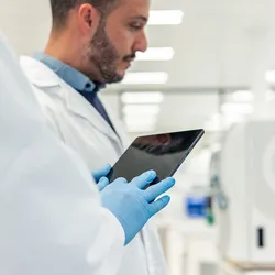 Two scientists wearing lab coats and gloves are using a digital tablet in a modern laboratory, conducting medical research with advanced equipment