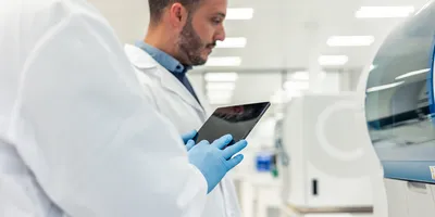 Two scientists wearing lab coats and gloves are using a digital tablet in a modern laboratory, conducting medical research with advanced equipment