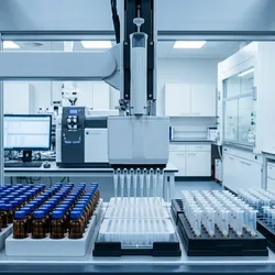 A modern automated liquid handling robotic workstation in a clean, professional laboratory, featuring an 8-channel pipette head processing samples above a 96-well plate, with rows of blue-capped amber glass vials in the foreground and clinical LC-MS analytical equipment in the background.