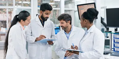 Four scientists in the lab meeting and looking at documents on clipboards