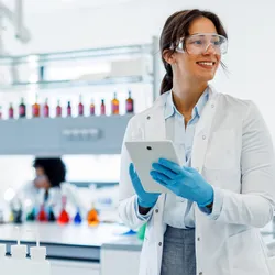 Scientist wearing a lab coat and gloves is using a digital tablet in a modern laboratory