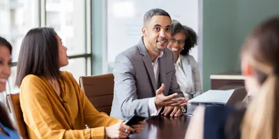 Group of colleagues sitting around conference table, with one male using influence and persuasion to pitch a business case