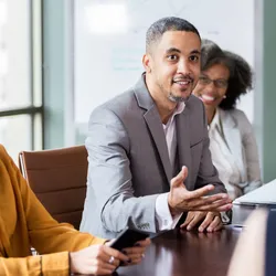 Group of colleagues sitting around conference table, with one male using influence and persuasion to pitch a business case