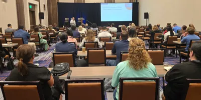 View of the back of a conference room filled with attendees listening to a Leadership Summit presentation.