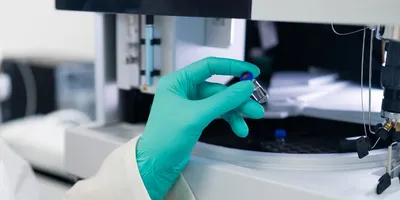Close up woman scientist in rubber gloves puts the vial to HPLC system with auto sampler.
