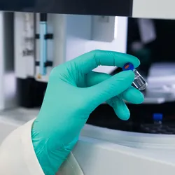 Close up woman scientist in rubber gloves puts the vial to HPLC system with auto sampler.
