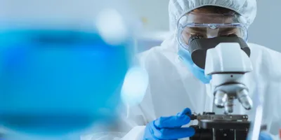 Researcher focused on microscope, wearing protective equipment.