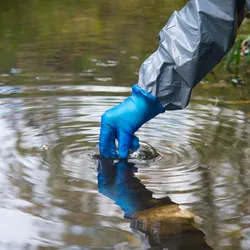 hand scientist, in a protective suit and gloves, collects water in a glass tube for testing