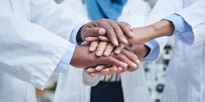 Shot of a group of unrecognisable scientists joining hands in solidarity in a laboratory