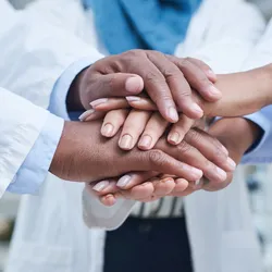 Shot of a group of unrecognisable scientists joining hands in solidarity in a laboratory