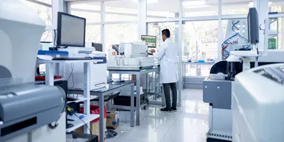 African American scientist doing some research at a laboratory and using a computer. The laboratory shows a variety of specialized equipment, demonstrating successful capital investment proposals