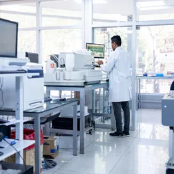 African American scientist doing some research at a laboratory and using a computer. The laboratory shows a variety of specialized equipment, demonstrating successful capital investment proposals