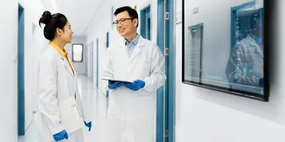 Two lab professionals discuss quality and operations in a laboratory corridor.