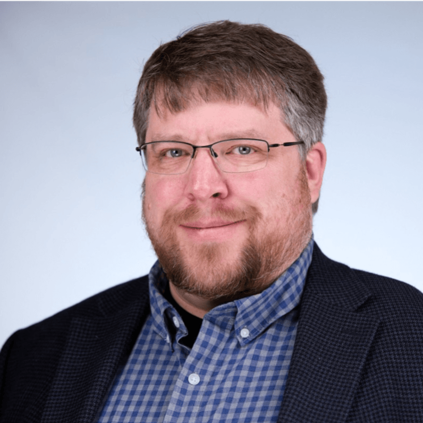 A professional headshot of a smiling man wearing a blazer. A professional headshot of a smiling man wearing a blazer.