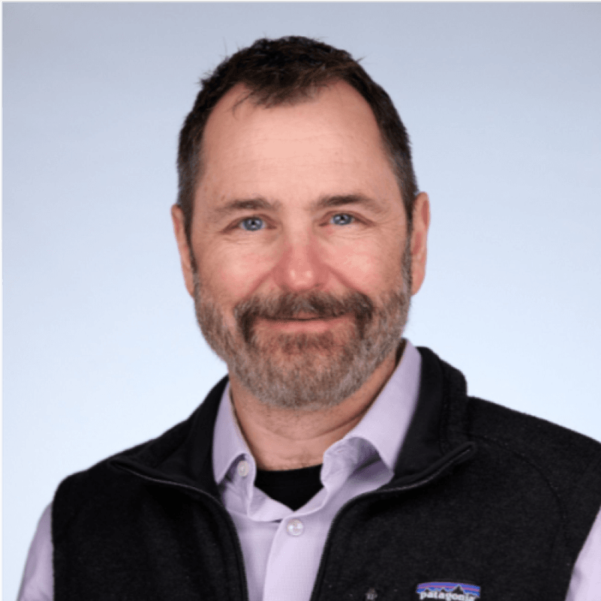 A white man with facial hair smiles in a headshot. A white man with facial hair smiles in a headshot.