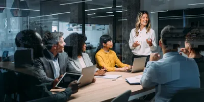 Female leader standing in conference room, advocating for the lab's priorities in front of seated executive colleagues